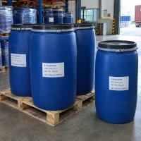 Blue plastic drums labeled 4-Vinylaniline (4-Aminostyrene) CAS 1520-21-4 with 200 kg net weight on a wooden pallet in a warehouse with racks and a container truck in the background.