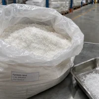 Open white woven bag showing white Cyanuric Acid crystals CAS 108-80-5 with a stainless steel tray of crystals beside it in a warehouse.
