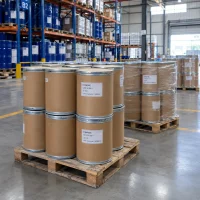 Stacked 25kg brown fiber drums of D-Ribose CAS 50-69-1 on wooden pallets in a warehouse, some shrink-wrapped, with racks of blue drums behind.