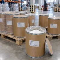 Open fiber drum showing white D-Ribose powder CAS 50-69-1 with its lid beside, among stacked 25kg drums on pallets in a warehouse with a forklift behind.
