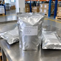 Three silver foil bags of Hydrolyzed Sclerotium Gum CAS 39464-87-4, 1kg net weight, standing on a stainless steel table in a warehouse.