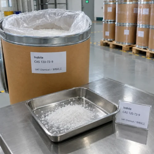 Indole (CAS 120-72-9) white crystalline flakes in a stainless steel tray beside an open fiber drum with liner