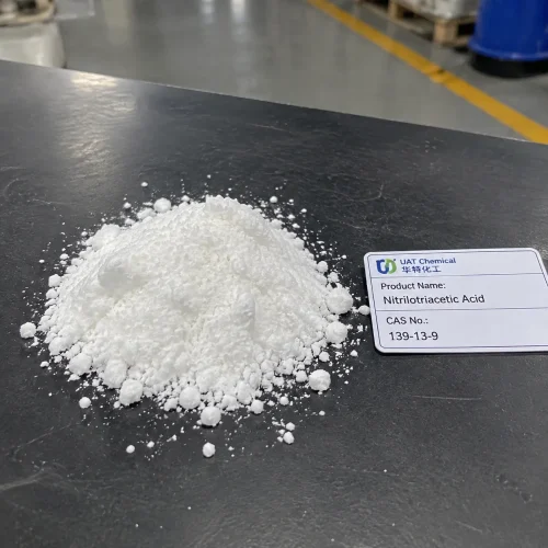 Pile of white Nitrilotriacetic Acid NTA powder CAS 139-13-9 on a dark table with a product label card in a factory.