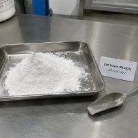 Pile of white Zinc Borate ZB-2335 powder CAS 12767-90-7 in a stainless steel tray with a product label and a metal scoop on a table.