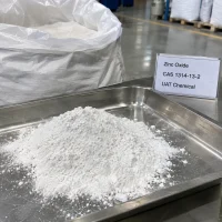 zinc-oxide-zno-cas-1314-13-2-white-powder-sample-tray Pile of white Zinc Oxide ZnO powder CAS 1314-13-2 in a stainless steel tray with a product label, beside an open woven bag of powder in a warehouse.